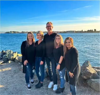 Dr. Michael Teichman, a Concord-based orthodontist, stands outdoors by a body of water with four members of his professional dental team, all smiling and dressed in black.